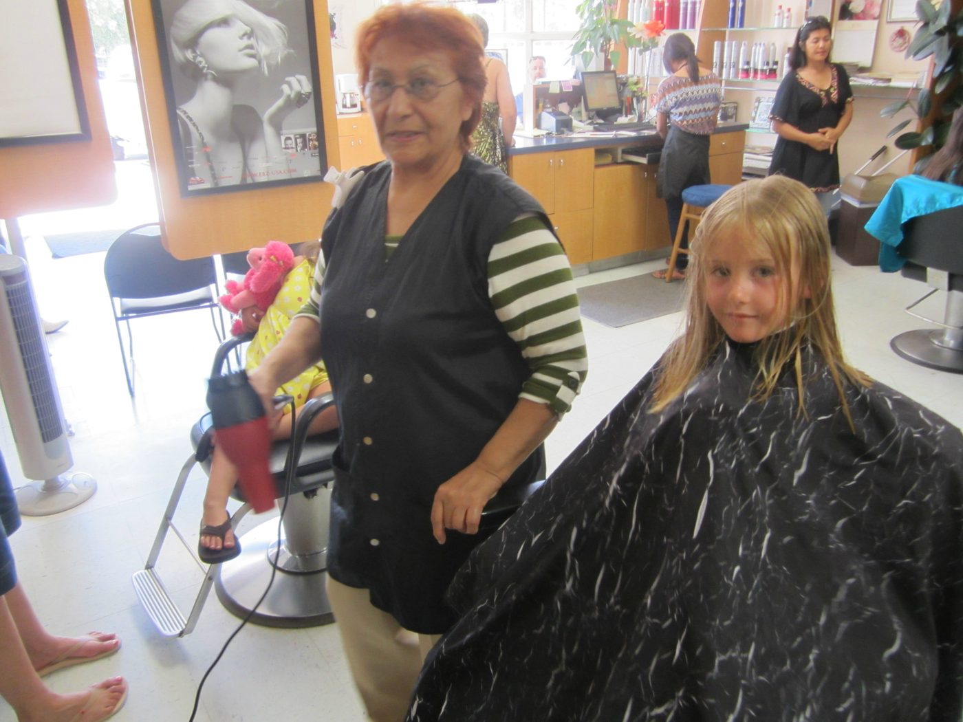 Stylist finishing a young girl's haircut with a blow dryer